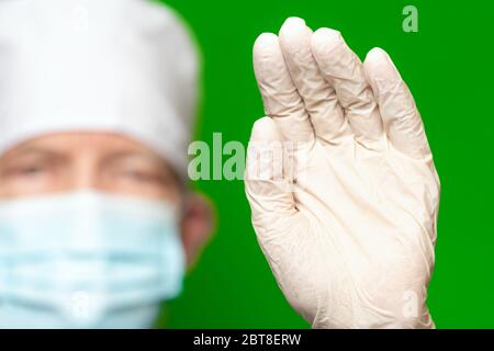 Médecin de sexe masculin en chirurgie masque facial sur le premier plan de flou artistique a mis la paume de sa main en avant-plan gant médical de protection, fait un bruit de main Banque D'Images