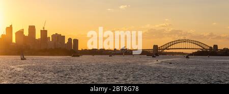 Vue panoramique sur le centre-ville de Sydney, le pont du port et l'opéra avec des bateaux naviguant dans la baie au coucher du soleil. Magnifique ciel orange. Banque D'Images