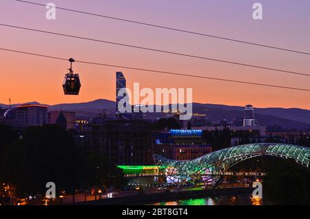 Tbilissi : coucher de soleil sur le pont de la paix, avec un téléphérique traversant la rivière Kura (République de Géorgie) Banque D'Images