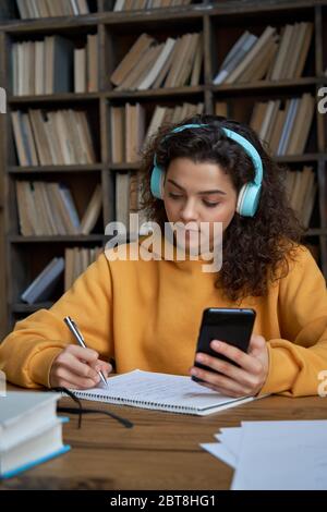 Hispanique fille vêtements écouteurs tenir téléphone à distance apprentissage dans l'application mobile. Banque D'Images