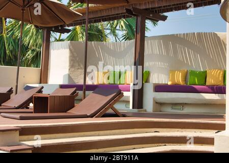 Cette photo unique montre une piscine avec des chaises longues et des parasols et un siège avec des coussins décoratifs colorés. La photo a été prise en Thaïlande Banque D'Images