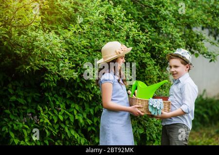 Gardenier souriant, adorable fille et blond, tenant le panier et les outils horticoles dans le jardin par beau temps. En été Banque D'Images