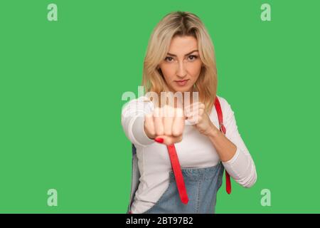 Lutte contre la menace. Portrait d'une femme blonde adulte courageuse et confiante dans une combinaison élégante en denim, qui bat et enrache les poings pour repousser les attaques. Dans Banque D'Images