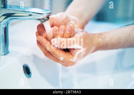 L'homme lave la mousse de ses mains à l'eau du robinet qui s'écoule dans le lavabo blanc. Propreté et hygiène. Banque D'Images