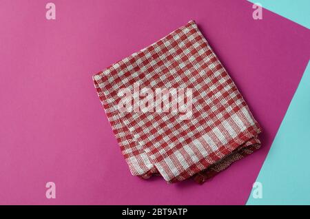 Fond rose clair avec une serviette à carreaux blanche et rouge. Serviette de cuisine pliée sur une table de couleurs. Arrière-plan minimaliste pour le multitâche. Vue de Banque D'Images