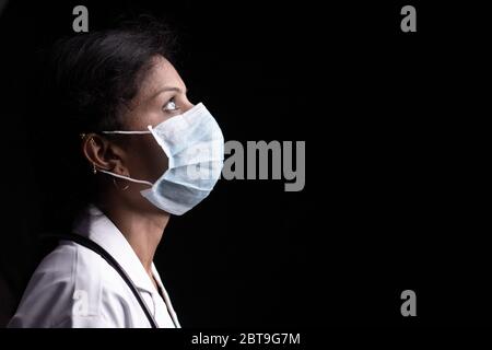 Profil de la jeune femme médecin avec les yeux ouverts dans le masque médical sur fond noir regardant vers le haut - concept d'espoir et de lutte pour mettre fin au coronavirus ou Banque D'Images