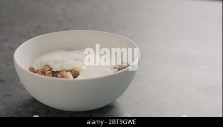 yaourt sur la granola au chocolat dans un bol blanc sur la surface de terrazzo Banque D'Images