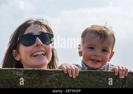 Mère et enfant jouant Peek-a-boo avec la caméra sur la plage: West Wittering, West Sussex, Angleterre, Royaume-Uni. MODÈLE LIBÉRÉ