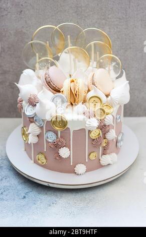 Gâteau d'anniversaire brun clair et doré avec macarons, pièces de monnaie, meringue et sucettes sur fond gris. Banque D'Images