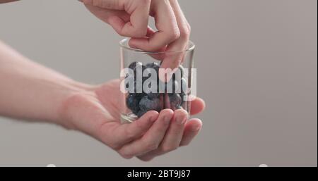 les mains d'homme prennent les bleuets mûrs humides lavés du pot en verre sur fond neutre Banque D'Images