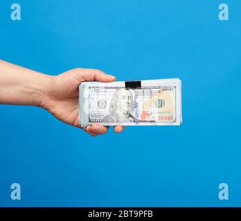 Main féminine tient une pile de papier dollars américains sur fond bleu, concept de pot-de-vin, salaire Banque D'Images
