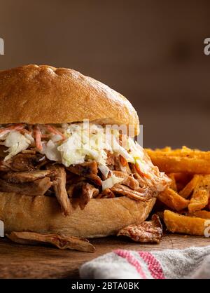 Gros plan d'un sandwich au poulet barbecue avec coleslaw sur un petit pain avec frites en arrière-plan sur un plan de découpe en bois rustique et un espace de copie Banque D'Images