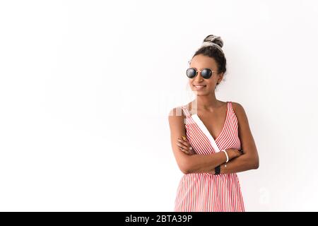 Photo d'une jeune femme africaine positive et optimiste souriante avec des semelles isolées sur fond de mur blanc portant des lunettes de soleil. Banque D'Images