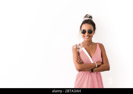 Image d'une jeune femme africaine optimiste et souriante avec des semelles isolées sur fond de mur blanc portant des lunettes de soleil. Banque D'Images