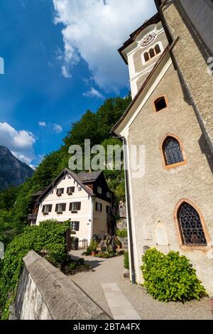 Le cimetière entourant l'église paroissiale de Hallstatt, région de Salzkammergut, OÖ, Autriche, avec une maison autrichienne traditionnelle à côté de l'entrée Banque D'Images