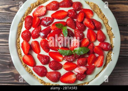 Cheesecake aux fraises avec feuilles de basilic, dans un plat de cuisson en céramique rouge sur fond de bois Banque D'Images