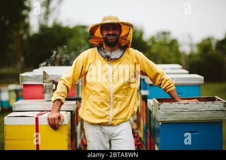 Portrait d'un gardien de beekeeper souriant entouré de ruches Banque D'Images