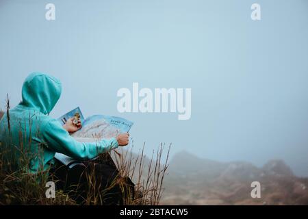 Voyageur avec une carte assis sur la colline d'une montagne en face d'une vue panoramique magnifique sur la vallée Banque D'Images