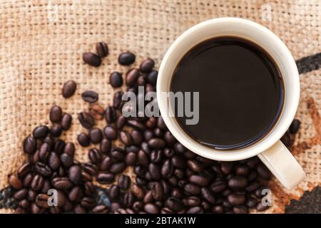 Tasse de café et grains de café rôtis sur le tissu du sac de jute. Photo d'arrière-plan de la vue de dessus Banque D'Images