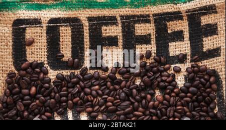 Les grains de café rôtis sont sur un sac en jute avec un texte noir standard de marque Coffee. Photo à plat, arrière-plan de la vue de dessus Banque D'Images