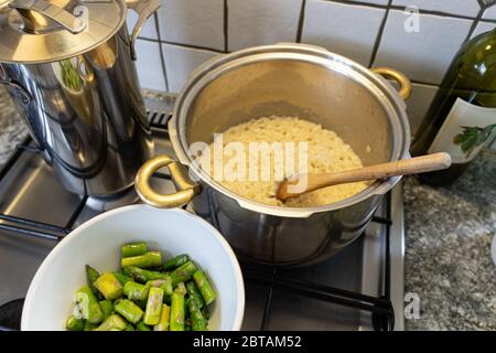 Cuisson d'un peu de riz risotto avec asperges, oignons et vin blanc. Émincé d'asperges dans un bol devant la casserole avec du riz. Vue grand angle. Banque D'Images