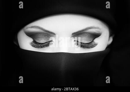 Portrait noir et blanc de la belle jeune fille asiatique/femme avec niqab mettant en valeur le maquillage et les cils longs. Banque D'Images