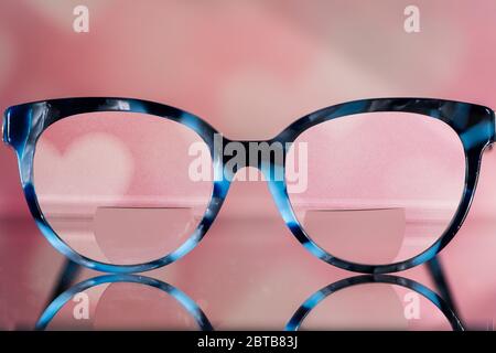 Lunettes de vue avec des bifocals et noir et bleu cadre vue brouillée agaist un fond rose flou avec des coeurs blancs. Concept de vision floue Banque D'Images