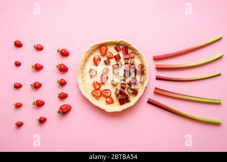 Faire une tarte aux fruits avec rhubarbe et fraises sur fond rose, au-dessus de la vue. Tarte à la fraise-rhubarbe, étape par étape. Banque D'Images