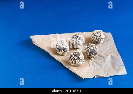 Cinq boules d'énergie faites maison dans du papier d'emballage sur une table bleue. Un dessert au chocolat maison sain pour le petit déjeuner vous remplira d'énergie. Arrosage d'écrous Banque D'Images