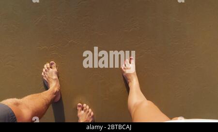 pieds nus couple marche le long de la plage de sable humide pour nettoyer l'eau de l'océan laver les jambes le jour ensoleillé proche vue du premier point supérieur Banque D'Images