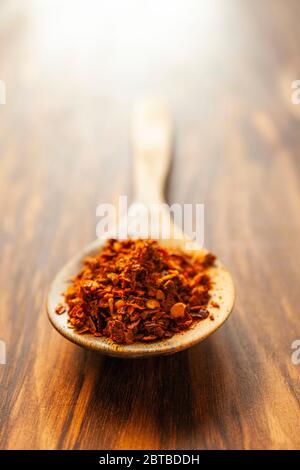 Poivrons de Chili écrasés épicés séchés sur une cuillère en bois. Photo verticale avec beaucoup d'espace libre. Banque D'Images