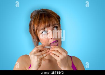 Une jeune femme heureuse roule une cigarette sur un fond bleu Banque D'Images