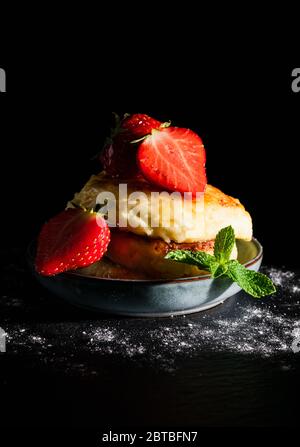 des cheesecakes encore à vie avec des fraises et une feuille de menthe, arrosées de miel sur fond noir Banque D'Images