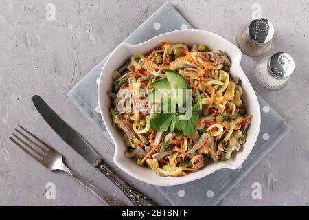 Salade avec coeurs de poulet, concombres, carottes, oignons et petits pois dans un bol blanc sur fond de béton gris, format horizontal, vue de dessus, gros plan Banque D'Images