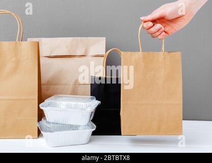 Service de livraison de nourriture. Emballage de sac en papier marron artisanal dans la main femelle. Emballage de maquette de livraison. Récipients en papier d'aluminium et emballages en papier gris table Banque D'Images