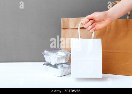 Sac en papier blanc artisanal à main femelle. Emballage de maquette de livraison. Récipients de feuilles alimentaires et emballages en papier sur fond gris de table. Livraison de nourriture Banque D'Images