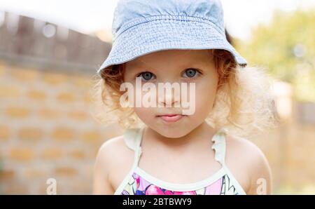 Joli portrait de petite fille enfant en denim bleu panama en été. Blonde curvy caucasien triste, fille sérieuse. Bonne enfance en été Banque D'Images