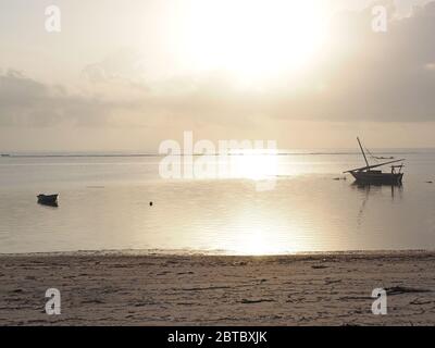 Petit bateau de pêche et bouée traditionnelle à marée basse dans l'argent clair tôt le matin lumière avec plage déserte à Malindi, Kenya Coast, Afrique Banque D'Images