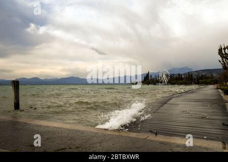 Vue panoramique sur le lac pendant une tempête avec de hautes vagues qui inondent la jetée en bois de la promenade, Bardolino, Vérone, Vénétie, Italie Banque D'Images