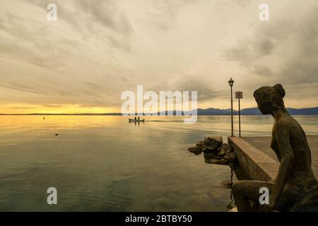 'La petite sirène' (2018), statue en bronze de l'artiste Libero Cecchini, sur le bord du lac de Lazise avec un bateau de pêche au coucher du soleil, Vérone, Italie Banque D'Images