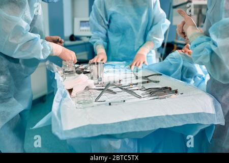 Instruments stériles sur la table d'opération, une équipe de médecins présente les instruments pour l'opération. De nombreuses mains sont en train de préparer des gants stériles. Banque D'Images