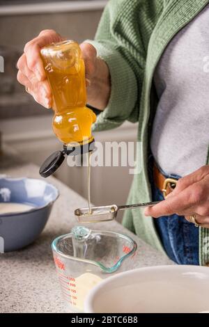 Femme versant du miel dans une tasse de beurre, en préparation pour faire du pain de blé germé Banque D'Images