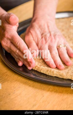 Une fois que la pâte à pizza a été étirée autant que possible dans l'air, aplatissez-la avec vos mains, en commençant au centre et en travaillant vers l'extérieur, utilisez y Banque D'Images