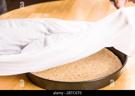 Après avoir étirée la pâte à pizza multigrains pour l'adapter à la casserole, laissez la croûte lever pendant au moins une demi-heure, en la recouvrant d'un chiffon humide, avant baki Banque D'Images