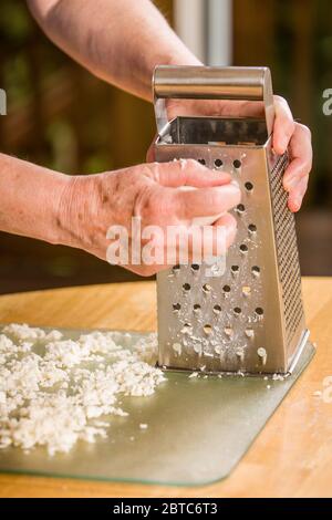 Femme râpant le fromage mozzarella étant étalé à sécher avant d'être utilisé comme garniture de pizza Banque D'Images