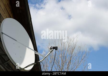 Plat satellite sur une maison de campagne sur un fond de ciel bleu avec des nuages. L'importance des télécommunications dans la période d'auto-isolement. Banque D'Images