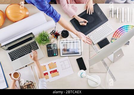 Équipe de designers d'intérieur travaillant sur des projets à grande table avec des ordinateurs, des règles et des palettes de couleurs Banque D'Images