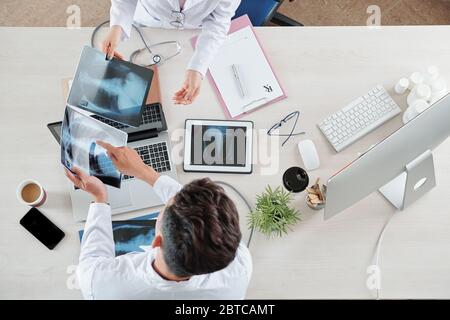 Les médecins assis à table et discutant des radiographies thoraciques des patients atteints de pneumonie, vue d'en haut Banque D'Images