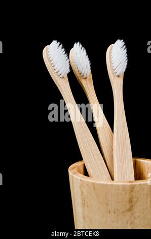 Brosses à dents en bambou dans une tasse en bois sur fond noir, concept zéro déchet. Banque D'Images