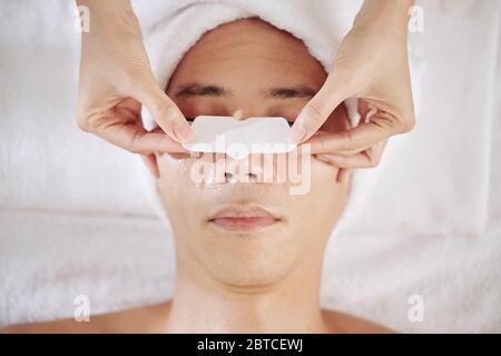 Cosmétologue appliquant la bande de nez sur le nez du jeune homme pour éliminer les pores Banque D'Images